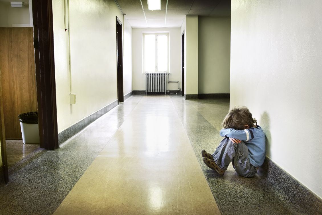 Yksinäinen lapsi istumassa koulun käytävällä. 